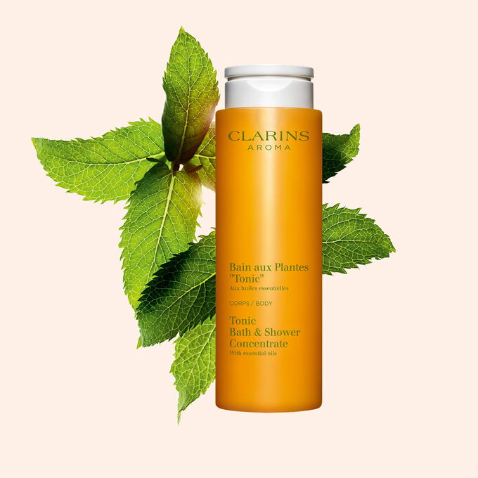 Packshot of Clarins Tonic Bath and Shower Concentrate gel, close to some mint and rosemary leaves on an orange background.
