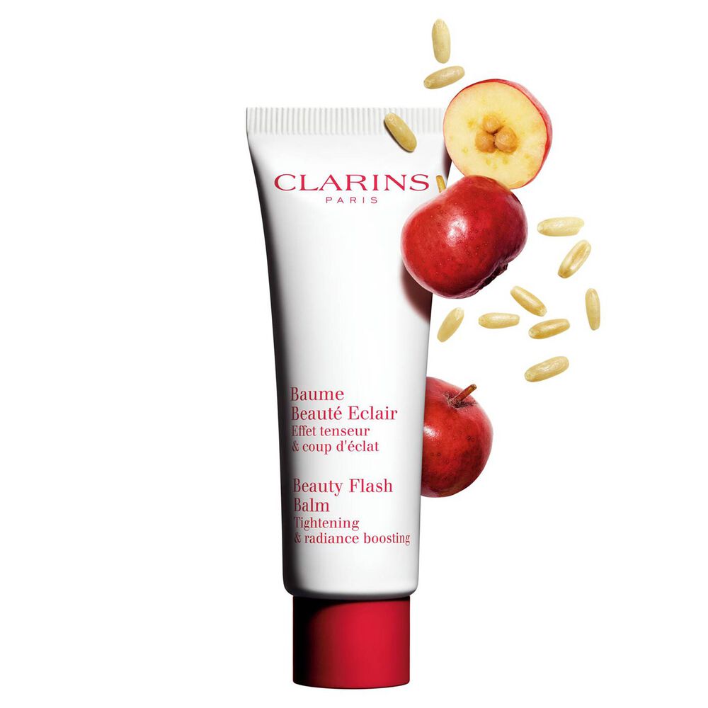 Packshot of a tube of Clarins Beauty Flash Balm close to acerola berries on a peach background.