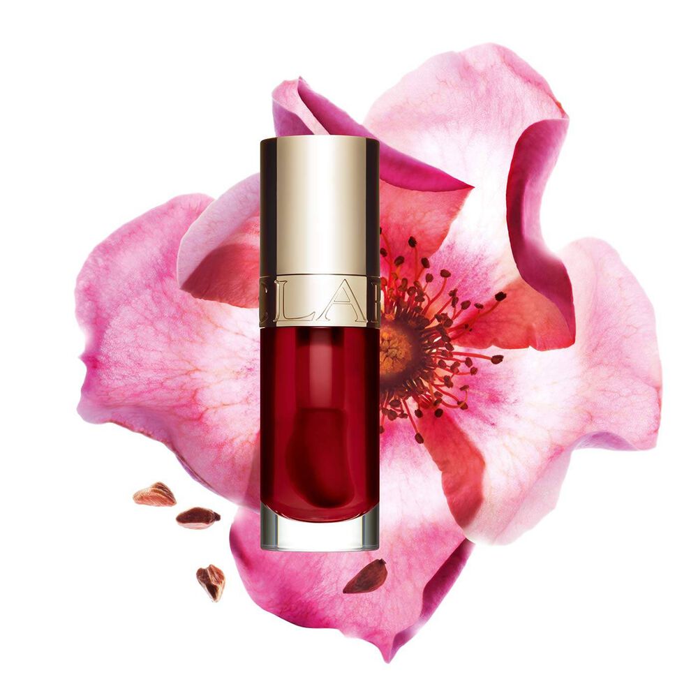 Packshot of Clarins Lip Comfort Oil in Cherry, placed next to a sweetbriar rose on a light pink background.