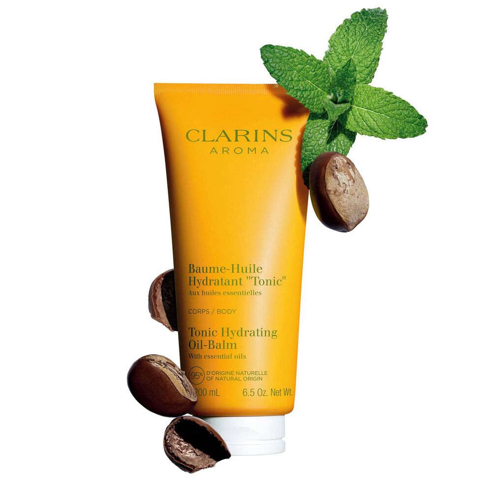 Packshot of a tube of Clarins Tonic Hydrating Oil-balm, close to some mint leaves and shea nuts on a peach background.