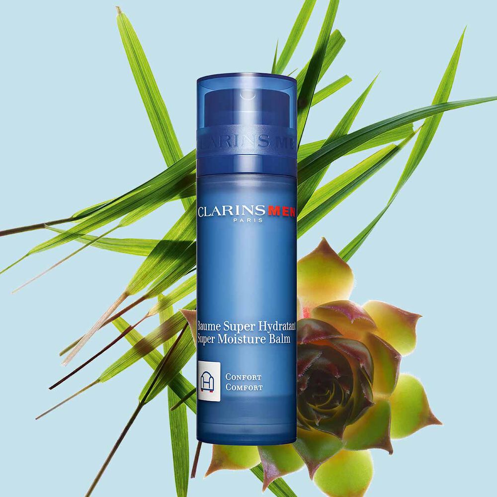 Packshot of a pump bottle of Clarins Men Super Moisture Balm close to gymnena and bison grass on a blue background.
