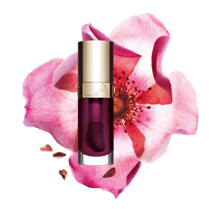 Packshot of Clarins Lip Comfort Oil Plum, placed next to a sweetbriar rose on a light pink background.