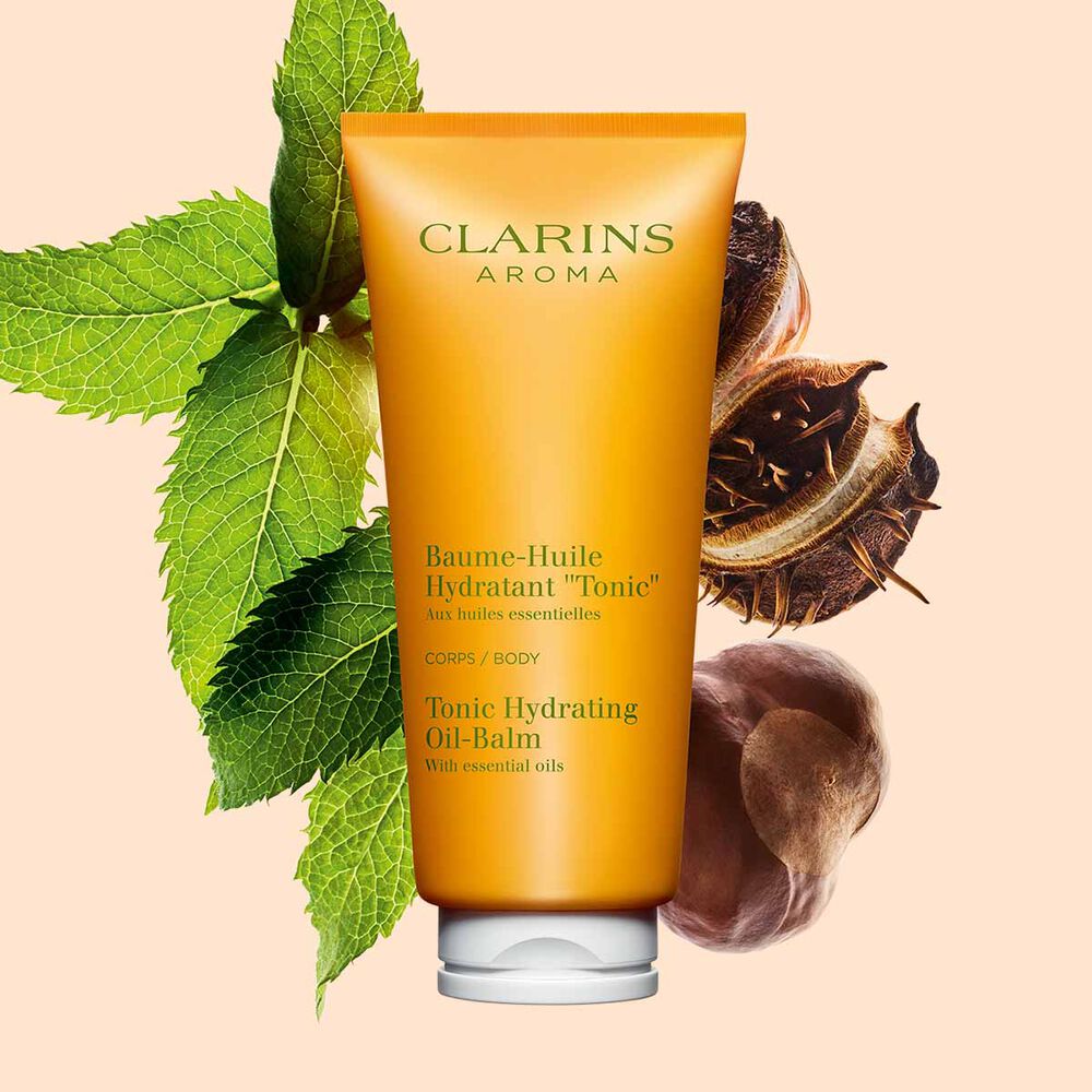 Packshot of a tube of Clarins Tonic Hydrating Oil-balm, close to some mint leaves and shea nuts on a peach background.