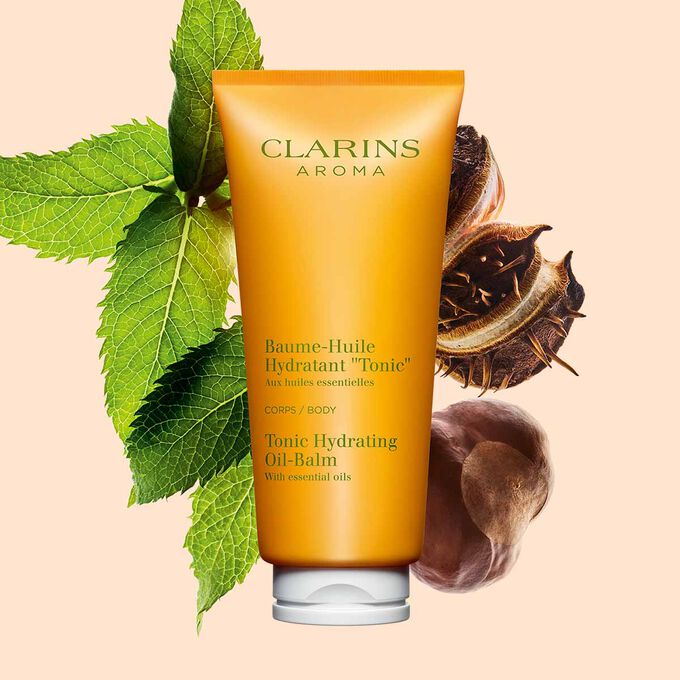 Packshot of a tube of Clarins Tonic Hydrating Oil-balm, close to some mint leaves and shea nuts on a peach background.
