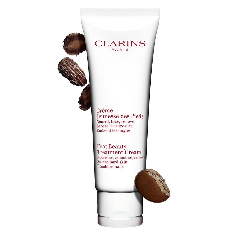 Packshot of a bottle of Clarins Foot Beauty Treatment Cream close to some shea nuts on a white background.