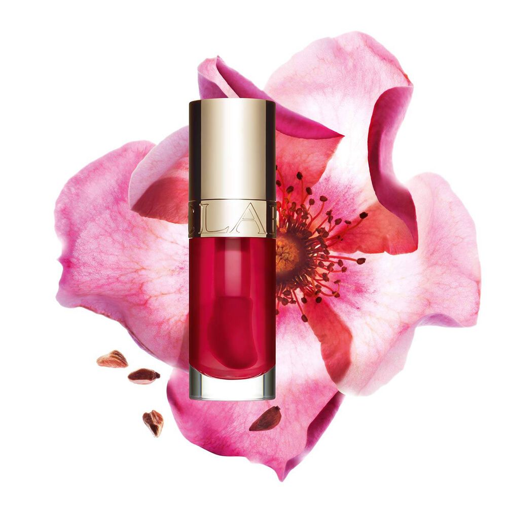 Packshot of Clarins Lip Comfort Oil Fushia, placed next to a sweetbriar rose on a light pink background.