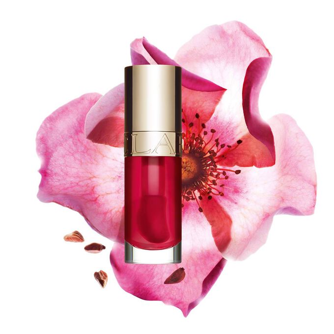 Packshot of Clarins Lip Comfort Oil Fushia, placed next to a sweetbriar rose on a light pink background.