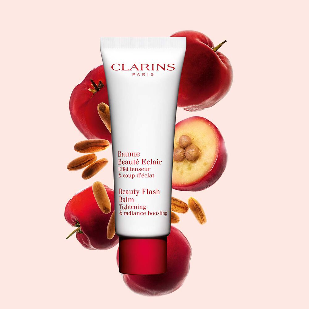 Packshot of a tube of Clarins Beauty Flash Balm close to acerola berries on a peach background.