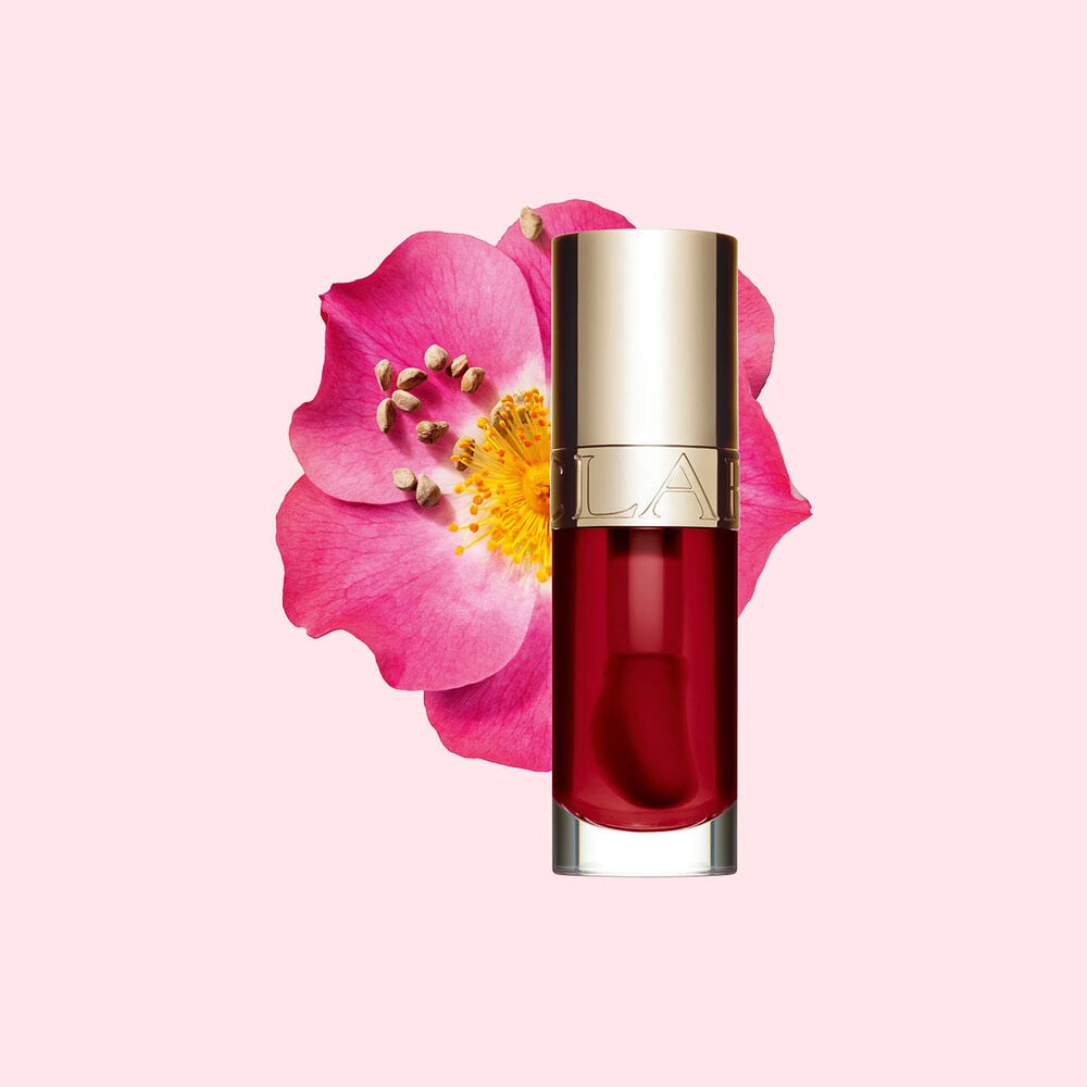 Packshot of Clarins Lip Comfort Oil in Cherry, placed next to a sweetbriar rose on a light pink background.