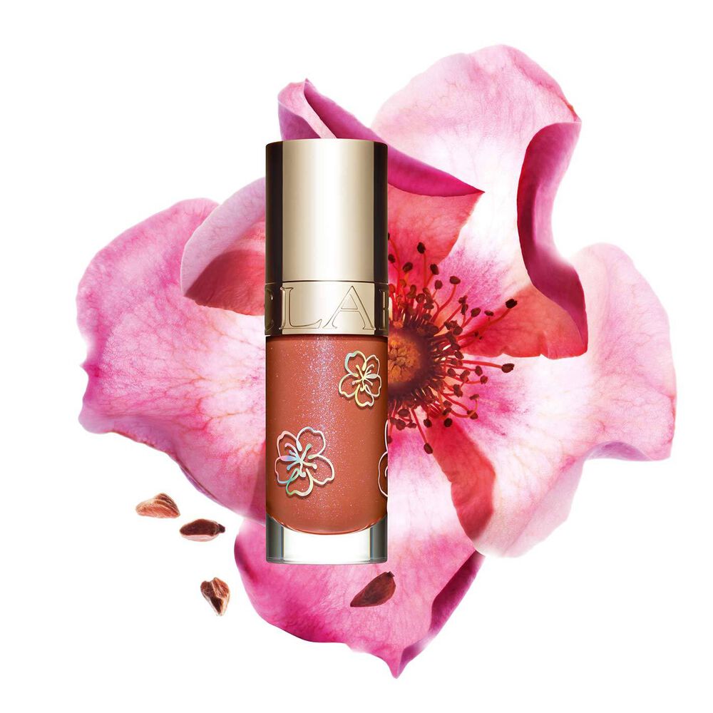 Packshot of Clarins Lip Comfort Oil in Rosy Sakura, a limited edition lip product in a pink shade, next to a flower.