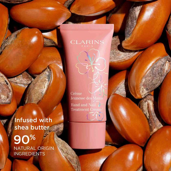 Packshot of Clarins Fairy Blossoms Hand Cream surrounded by shea butter seeds, highlighting its 90% natural origin formula.
