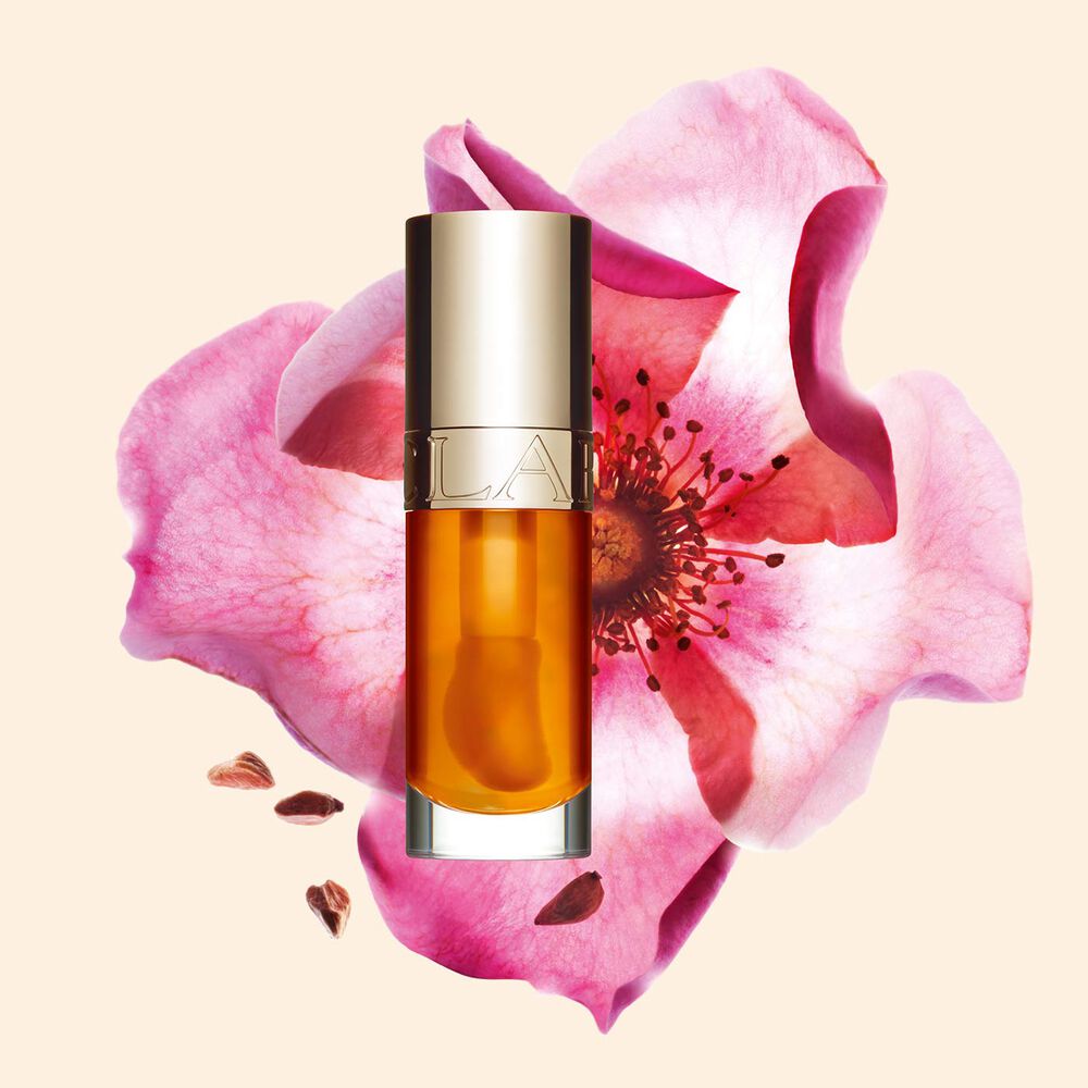 Packshot of Clarins Lip Comfort Oil in Honey, placed next to a sweetbriar rose on a light peach background.