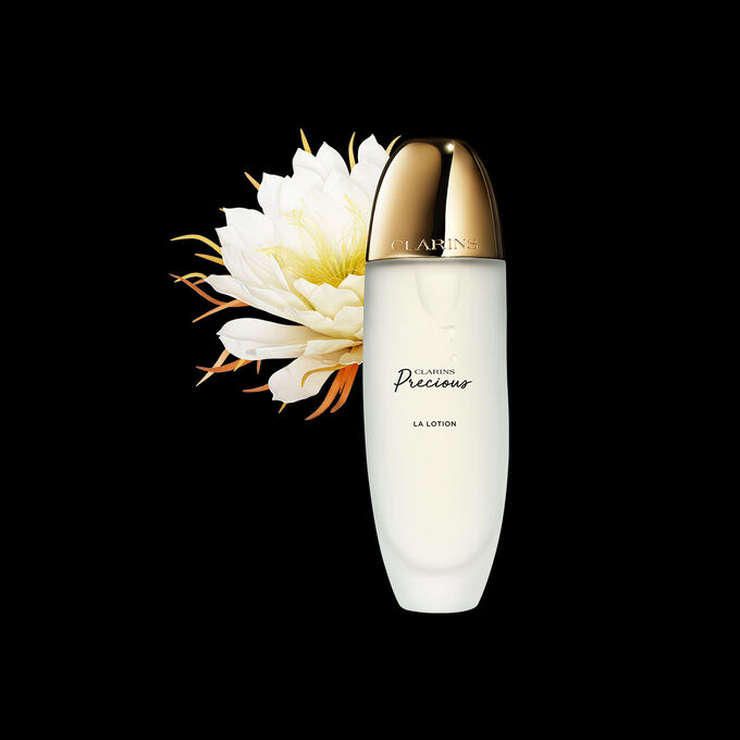 Packshot of Clarins Precious Treatment Essence close to a Moonlight flower on a dark background.