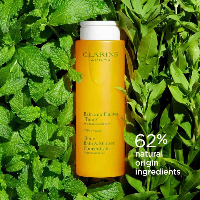 Bottle of Clarins Tonic Bath and Shower Concentrate among mint and rosemary leaves, to illustrate its natural ingredients.