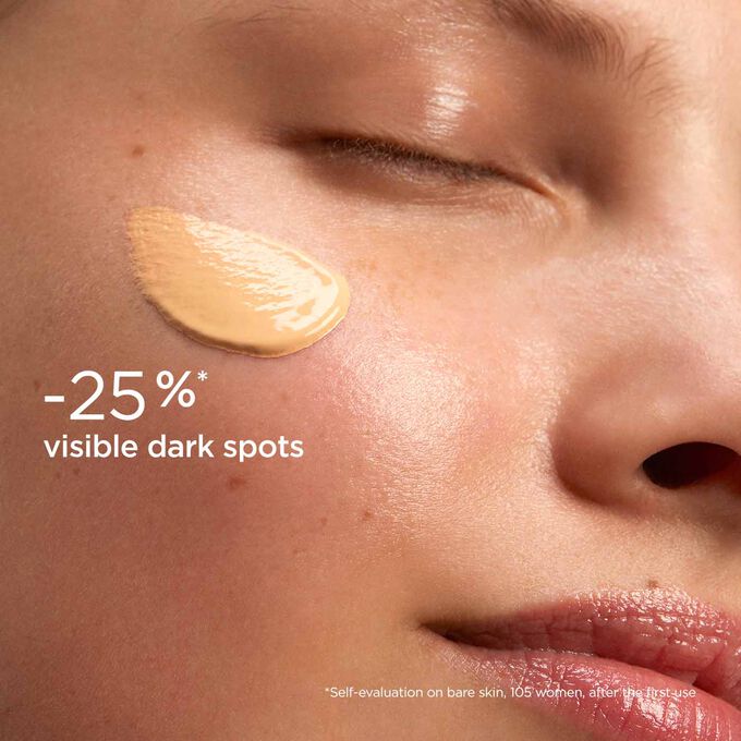 Woman wearing SOS Primer Peach by Clarins to illustrate that it reduces dark spots by 25%.